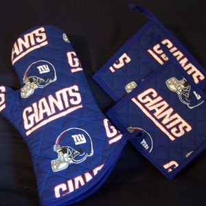 May include: A blue quilted oven mitt and two matching pot holders. The set features the word "GIANTS" in white block letters, along with a football helmet graphic. The design is repeated across the items.