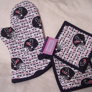 May include: A set of two white and navy blue oven mitts with a quilted design. The mitts feature a repeated pattern of the Houston Texans logo, which includes a red star and the words "Houston Texans". The mitts are labelled "Stitchingram".