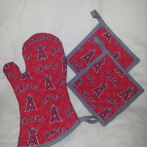 May include: Set of red and gray oven mitts and pot holders with a repeating pattern of the Los Angeles Angels baseball team logo. The logo features a red "A" with a halo above it and the word "Angels" written in white.