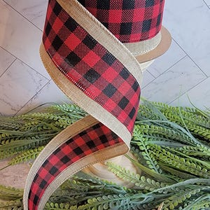 May include: A spool of wired ribbon featuring a red and black buffalo check pattern on a textured tan burlap base. The ribbon is wound around a cardboard core and cascades downward in a spiral, showcasing the woven fabric and finished edges.
