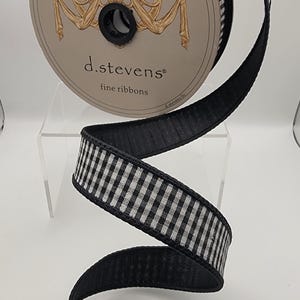 May include: A spool of d.stevens fine ribbons featuring a black and white gingham pattern. The ribbon has a solid black edge and is wound around a circular cardboard reel with a gold-colored decorative emblem and the brand name printed on it.