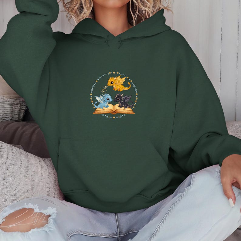 Pu&ograve; includere: Felpa con cappuccio verde scuro con un disegno circolare di tre draghi dei cartoni animati: giallo, blu e nero. Sono posizionati attorno a un libro aperto, all'interno di un cerchio punteggiato con stelle. La felpa ha una tasca a marsupio e un cappuccio.