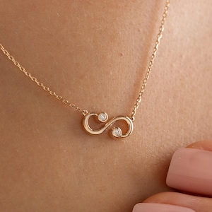 Puede incluir: Un delicado collar de oro con un colgante con forma de símbolo de infinito con dos pequeñas gemas brillantes. El colgante cuelga de una fina cadena. Una joya sencilla pero elegante.