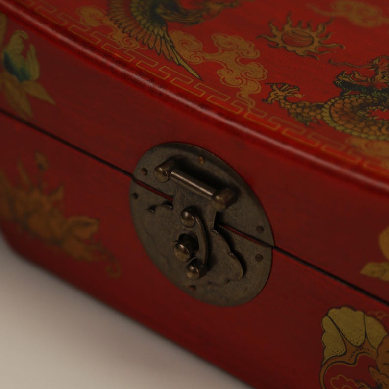 May include: A red wooden box with ornate gold dragon and bird designs. The box has a metal clasp and hinges. The design is reminiscent of traditional Asian art.