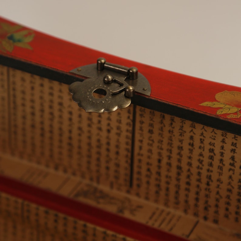 May include: Close-up of a red wooden box with a decorative brass clasp. The box features a floral design and is lined with pages of text. The clasp is ornate, adding a vintage aesthetic.