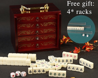 May include: A complete Mahjong set with a dark red wooden storage box featuring five drawers with gold dragon designs. The set includes ivory-colored tiles, dice, and a small dish. The image also includes the text "Free gift: 4* racks."