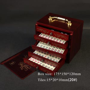 May include: A wooden mahjong set with a dark red finish. The set includes a box with four open drawers filled with tiles. The box has a gold handle and decorative carvings. The box size is 175*150*120mm, and the tiles are 15*20*10mm.
