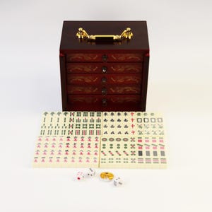 May include: A complete Mahjong set with a dark wood cabinet featuring five drawers and gold-colored hardware. The set includes ivory-colored tiles with red, green, and black markings, dice, and a gold-colored coin.