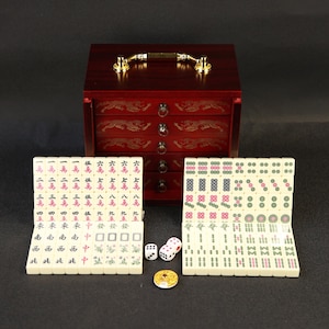 May include: A complete Mahjong set with ivory-colored tiles, dice, and a decorative coin. The set includes a wooden storage box with a handle and gold-colored hardware. The box and tiles feature Chinese characters and symbols.