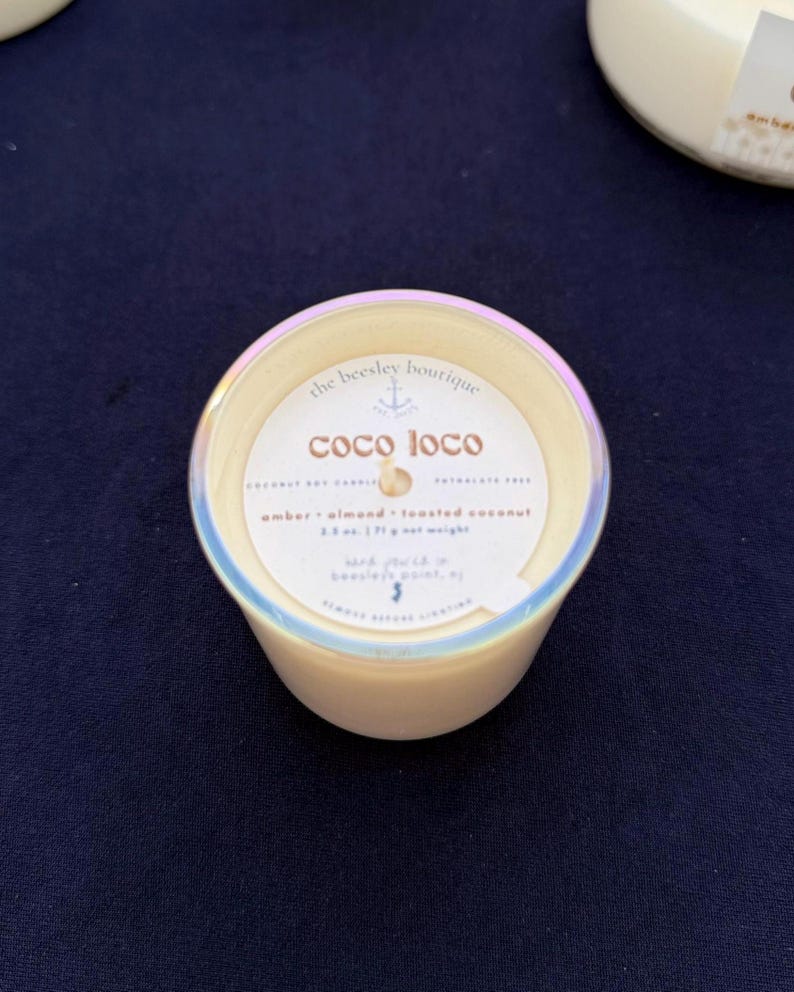 Puede incluir: Una vela peque&ntilde;a y redonda en un recipiente color crema con un borde hologr&aacute;fico. La etiqueta dice "coco loco" y enumera la fragancia como &aacute;mbar, almendra y coco tostado. El peso neto es de 71 g.