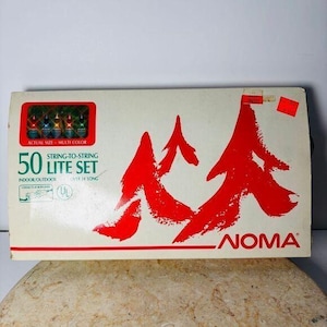 May include: A vintage box of NOMA 50 Lite Set string lights. The box is white with red accents and text. The text includes "50 Lite Set", "Indoor/Outdoor", and "Over 24' Long". A small window shows the multi-color lights.
