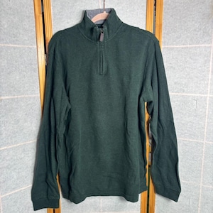 May include: A dark green long-sleeve pullover sweater with a ribbed texture and a quarter-zip closure. The sweater has a high collar with a gray lining. The sleeves are long and the fabric appears to be a medium weight.