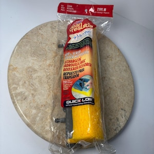 May include: A yellow mop refill in a clear plastic package. The package has red and white text that reads "Clean Results" and "Microban". The mop refill is cylindrical and has a textured surface. The mop refill is on a round, beige stone.