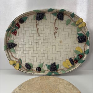May include: Oval woven tray with a cream-colored background and a decorative border of painted fruit and leaves. The fruit includes grapes, strawberries, and pears. The tray has a woven texture.