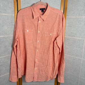 May include: A coral-colored button-down shirt with long sleeves, two chest pockets, and a collared neckline. The shirt is hanging on a wooden hanger. The brand name "Lands' End" is visible on the label.