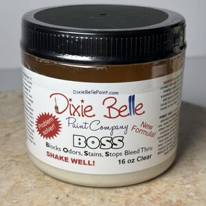 May include: A clear 16 oz jar of Dixie Belle Paint Company BOSS, a problem solver that blocks odors, stains, and stops bleed-through. The jar has a black lid and a white label with red and blue text.