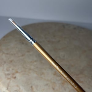 May include: A makeup brush with a gold handle and silver ferrule. The brush has a clear plastic cap protecting the bristles. The text "Bare Essentials" is printed on the handle.