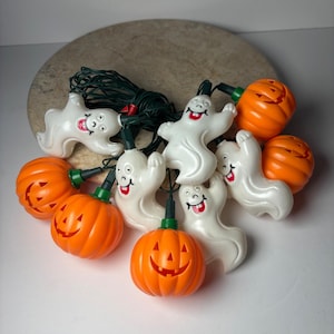 May include: A string of Halloween decorative lights featuring alternating white ghost figures and orange pumpkin jack-o'-lanterns. The ghosts have painted facial features with red mouths, and the pumpkins have carved-out faces on dark green wire.