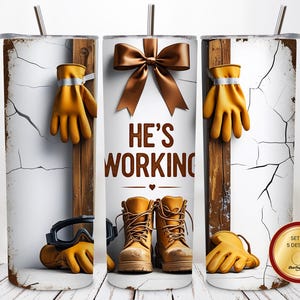 Könnte beinhalten: Set aus drei Edelstahlbechern mit einem Design, das Arbeitsstiefel, Handschuhe und Schutzbrillen zeigt. Der Text "HE'S WORKING" ist auf dem mittleren Becher zu sehen. Die Becher haben einen weißen Hintergrund mit Rissoptik.