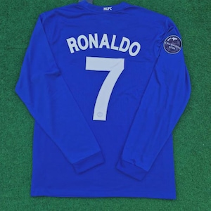 May include: Royal blue long-sleeve jersey with the name "RONALDO" and the number "7" in white. The jersey has "MUFC" printed at the top and a "CHAMPIONS 07/08" patch on the sleeve.