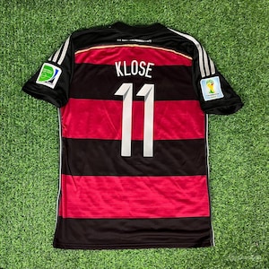 May include: Black, red, and white Germany soccer jersey with the name "KLOSE" and the number "11" on the back. The jersey has the FIFA World Cup logo on the sleeves and the German national team logo on the chest.