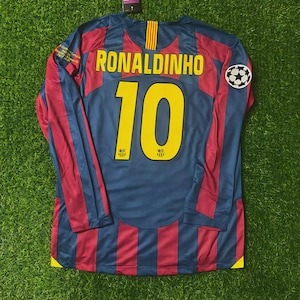 May include: A long-sleeved soccer jersey with the name "RONALDINHO" and the number "10" in yellow. The jersey is primarily blue with red vertical stripes and a soccer ball patch. The jersey has a yellow and red stripe on the back of the neck.