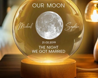 May include: A glowing glass sphere with a wooden base, featuring a detailed moon image. The sphere is inscribed with "OUR MOON," names "Michael" and "Sophia," and the date "21.02.2019," with the text "THE NIGHT WE GOT MARRIED."