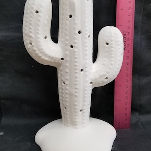 May include: White ceramic cactus figurine with a textured surface and holes throughout. The cactus is approximately 18 inches tall.