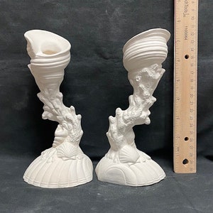 Puede incluir: Un par de candelabros de cerámica blanca con forma de conchas y coral. Los candelabros miden aproximadamente 18 cm de alto y tienen un tema rústico y costero.