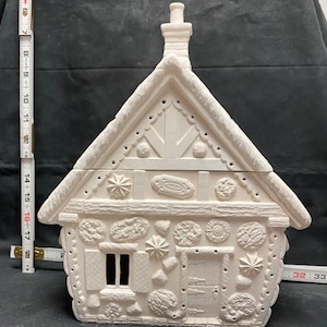 Puede incluir: Casa de jengibre de cerámica blanca con una chimenea y decoraciones detalladas de jengibre. La casa tiene dos ventanas y una puerta.
