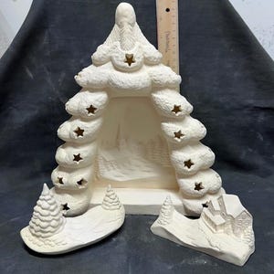 May include: A white ceramic Christmas tree with cut-out stars and a winter scene inside. The tree is in three pieces, with a base, a middle section, and a top. The base has a small house and two trees, while the middle section has a winter scene with trees and a snowy path. The top of the tree has a star on top.