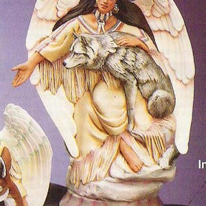 Puede incluir: Una figurita de porcelana de un ángel con alas, que lleva un vestido de inspiración nativa americana y sostiene un lobo. El ángel tiene el pelo largo y castaño y lleva un collar de cuentas. La figurita está pintada en tonos de blanco, marrón y dorado.