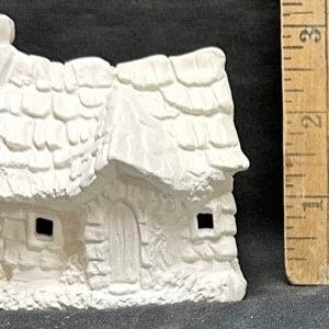 Może przedstawiać: Mały, niemalowany ceramiczny domek z teksturowanym, gontowym dachem i ścianami przypominającymi kamień. Domek ma drzwi, dwa okna i komin. Obok znajduje się drewniana linijka.