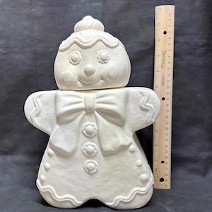 May include: White ceramic gingerbread man cookie jar with a bow and buttons. The cookie jar is ready to be painted.