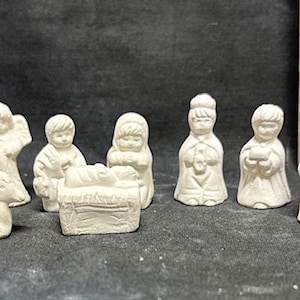 May include: A set of nine white ceramic figurines depicting the Nativity scene. The figures include Mary, Joseph, baby Jesus, an angel, a shepherd, a donkey, and a sheep. The figures are all in a standing position and are about 2 inches tall.