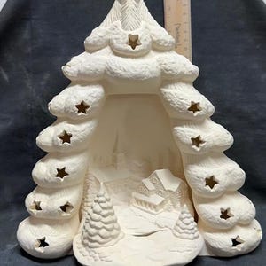 May include: White ceramic Christmas tree with cut-out stars and a winter village scene inside. The tree is hollow and can be used as a candle holder or a light-up decoration.