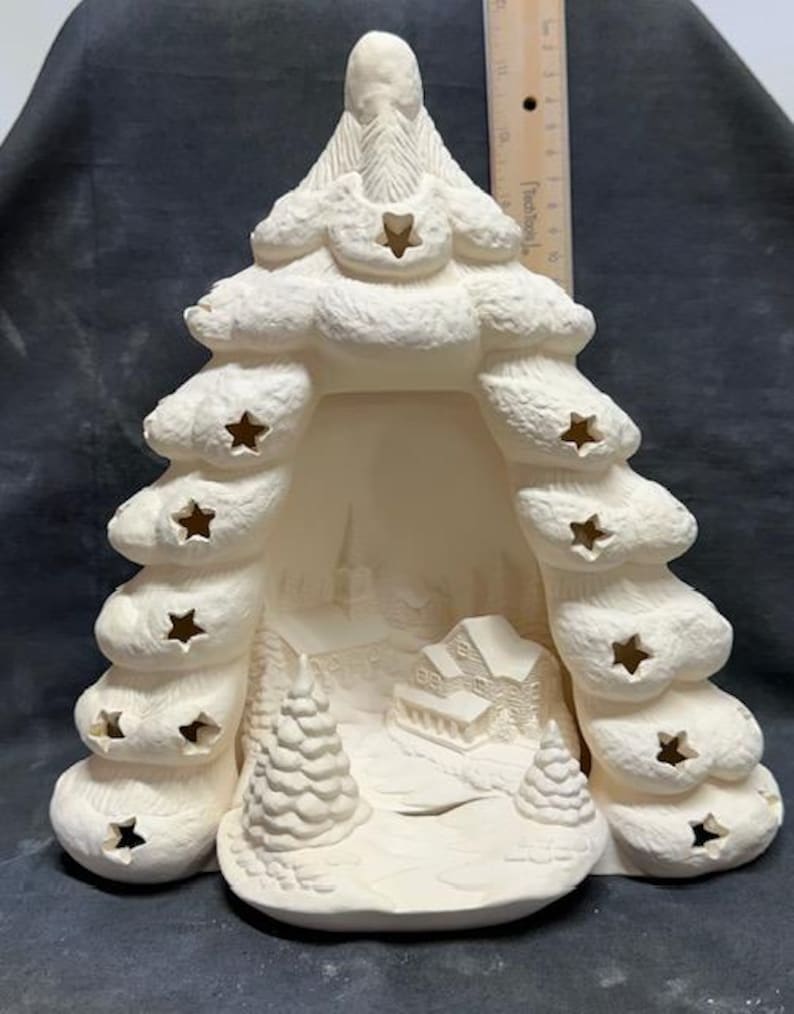 May include: White ceramic Christmas tree with cut-out stars and a winter village scene inside. The tree is hollow and can be used as a candle holder or a light-up decoration.