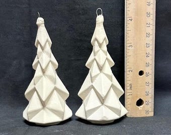May include: Two off-white, geometric Christmas tree ornaments. Each tree has a faceted design and a wire loop for hanging. A ruler shows the trees are approximately 4 inches tall. The background is a dark, solid color.