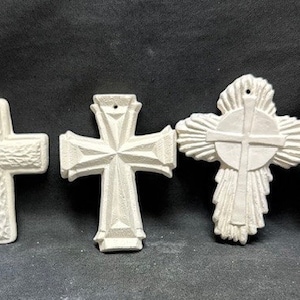 May include: Three white ceramic cross ornaments with different designs. The crosses are all about 4 inches tall.