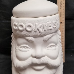 May include: White ceramic cookie jar shaped like Santa Claus's head with a lid. The jar has the word "COOKIES" written on the hat.