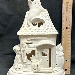 Könnte beinhalten: Weißes Keramik-Spukhaus mit einem Geist auf dem Dach, einem Kürbis auf jeder Seite und einem Schild mit der Aufschrift "1st Spook St."