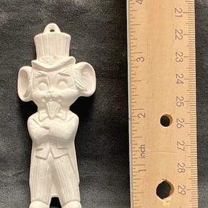 以下が含まれることがあります： 帽子とタキシードを着たネズミの白いセラミック製置物。ネズミは腕を組んで立っており、舌を出しています。置物は約7.6cmの高さです。