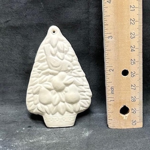 Può includere: Ornamento per albero di Natale in ceramica non rifinito, a forma di cestino di frutta. L'ornamento è alto circa 7.6 cm e ha un foro nella parte superiore per appenderlo. Un righello di legno è accanto all'ornamento.