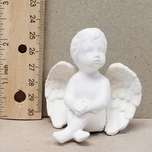 May include: White ceramic figurine of a sitting angel with wings. The angel has a cherubic face and is about 3 inches tall.