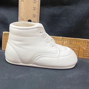 May include: White ceramic shoe-shaped planter with a lace-up design. The planter is approximately 7 inches long.