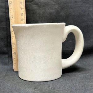 Peut inclure: Une tasse en céramique blanche avec une anse. La tasse est unie et prête à être peinte.