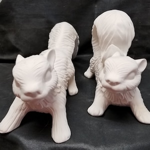 May include: Two white ceramic squirrel figurines. The squirrels are in a playful pose, with one standing on its hind legs and the other lying down with its head raised. The figurines are unpainted and ready to be decorated.