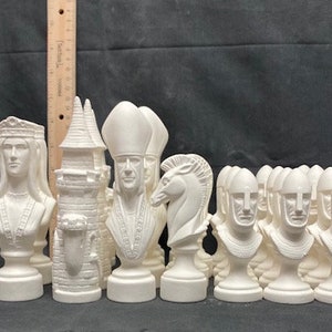 Puede incluir: Un conjunto de piezas de ajedrez de cerámica blanca, que incluye un rey, una reina, un alfil, un caballo, una torre y peones. Las piezas están sin pintar y listas para ser decoradas.