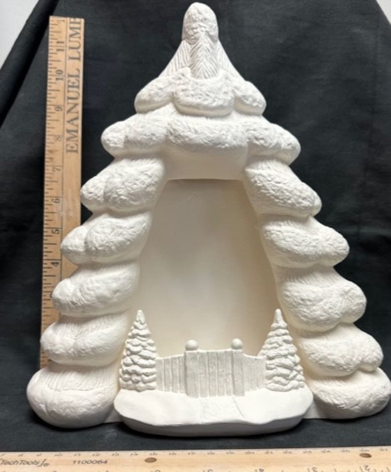 May include: White ceramic Christmas tree shaped picture frame with a snow-covered fence and two small pine trees at the base. The frame is ready to be painted.