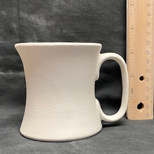 Puede incluir: Taza de cerámica blanca con una base ancha y acampanada y un asa. La taza mide aproximadamente 13 cm de alto.